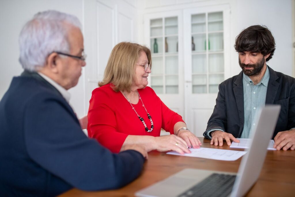 Seguro de salud sin complicaciones: deja que La Madrina del Papeleo te oriente Three business professionals in a meeting, discussing documents and planning strategies indoors.